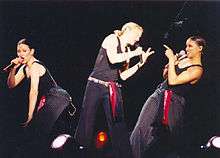 Madonna flanked by her dancers performing "Holiday". All of them wear black cloths.