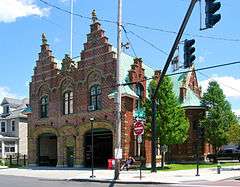 An ornate brick building with two large garages in front and two corresponding stepped point sections on the roof behind a traffic signal at the intersection of Delaware Avenue and Marshall Street, seen from the far corner.