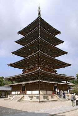 Wooden five-storied pagoda with white walls. Below the first roof, there is an additional attached pent roof.