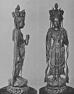 Front and profile view of a standing statue with her left arm bend forward. On the head there are small heads visible facing in various directions.