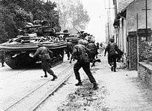 Sherman tanks and British soldiers advancing up a street