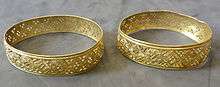 Two gold bracelets. They have the same geometric pattern, made by piercing many small holes into the gold