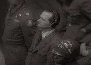 Lanz is seen at the Nuremberg Trials. He is heavily guarded and is wearing headphones.