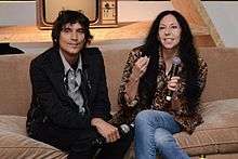 Inez and Vinoodh sitting on the sofa holding a mic.