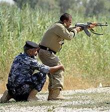 Soldier steadying another soldier who is firing a rifle