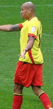 A man with bald hair who is wearing a yellow top, red shorts and red socks.