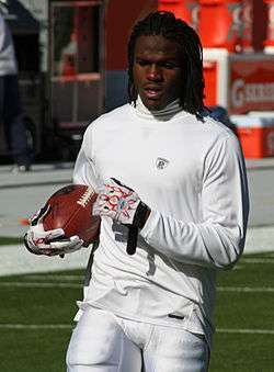 man in football pants and long-sleeved warm up shirt holding a football tucked in right arm