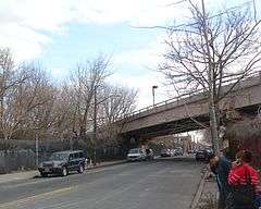 An elevated subway ramp for the BMT Jamaica Line above 130th Street in Richmond Hill, New York. The ramp descends into a tunnel portal to the left and ascends over a street to the right.