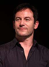 A man with short black hair and a black shirt, who is smiling.
