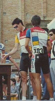 Two cyclists wearing the same jerseys while standing on a platform.