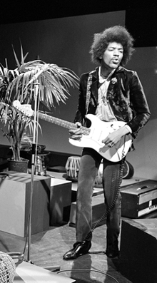 A black and white photograph of Jimi Hendrix playing a guitar