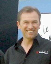 A smiling man in his forties wearing a black polo shirt with a wide lapel.