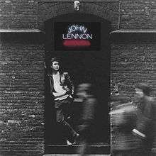 A black-and-white photo of Lennon leaning up against a brick wall
