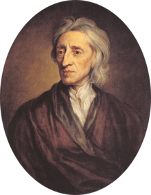 Three-quarter length portrait of a man with a shock of neck-length white hair wearing a loose brown robe and white shirt.