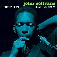 Coltrane leans back with a reed in his mouth in a deep blue-on-black photo. The words "BLUE TRAIN" are written above his head in white followed by "john coltrane" in orange.