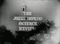Television screenshot looking up at the bell tower of a building through tall trees. The words "The Johns Hopkins Science Review" are superposed on the image.
