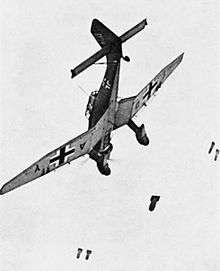 a black and white photograph of an aircraft releasing bombs from its wings and undercarriage in a dive