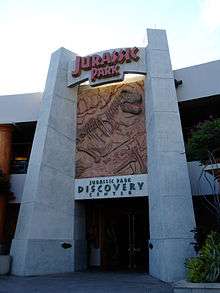 The gateway to a facility reading "Jurassic Park" at the top, "Discovery Center" at the bottom, and a rocky panel with a Tyrannosaurus skeleton in-between.