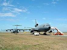 Two large gray jet aircraft on roomy ramp surrounded by grass, both angled away from the runway. The one closer to camera is three-engined, while the one further in the background is fourengined.