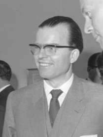 Black-and-white portrait of a man with glasses in semi profile wearing a suit and tie.