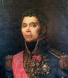 Portrait shows a curly-haired man with an oval face and small mouth. He wears an elaborate blue military uniform with many medals and gold braid.