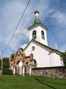 A Kihnu church with a green roof behind a small stone wall.