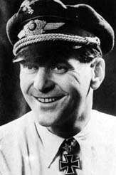 The head and shoulders of a young man, shown in semi-profile. He wears a peaked cap and shirt with an Iron Cross displayed at the front of his shirt collar. His hair appears dark and short, his nose is long and straight. He is smiling broadly; his eyes are looking to the left of the camera.