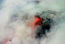 Photo showing clouds of steam surrounding lava that is partly black and partly glowing orange.