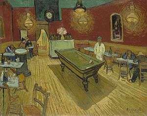A billiard table in the centre of a room of a cafe surrounded by tables. Patrons are seated at several tables, and a man dressed in white stands behind the billiard table.