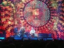 Robert Plant singing and Jimmy Page playing guitar in front of a large screen displaying an elaborate design.