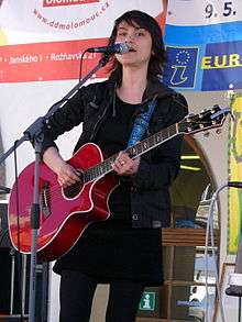 Young, dark-haired woman in black playing red acoustic guitar on stage