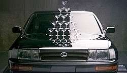 Car front view, halfway lit, with 15 champagne glasses stacked on the hood to form a triangle.