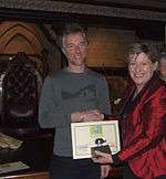 Minister Lianne Dalziel shaking Robert Ibell's hand and holding a certificate and a trophy