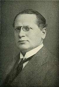 Portrait of a middle-aged man wearing glasses and a suit.