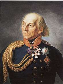 Painting shows a partially bald man with light-colored hair. He wears a dark blue military uniform with two rows of buttons, a large loop of gold braid over his shoulder and a large Iron Cross just below his chin.