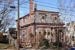 A small frame house with a mansard roof sided in clapboard painted a dusty shade of pink.