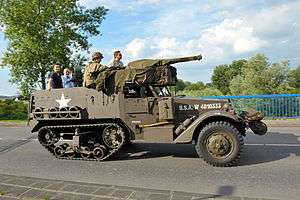 Several men and women riding a preserved M9 Half-track with a U.S. Army re-enactor.