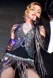 Madonna wearing a gray sparkly outfit, sings to a microphone in her hand.
