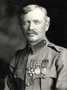 A black-and-white portrait photograph of a blond-haired white man in military uniform. He has a well-groomed moustache, bright eyes, sharply cut hair and a row of medals on his chest.