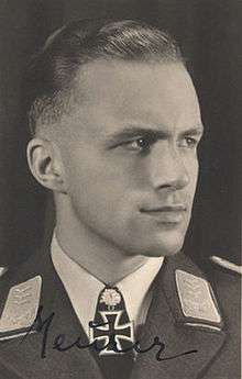 Black-and-white portrait of a man in semi profile wearing a military uniform with an Iron Cross displayed at his neck, his hair is combed back.