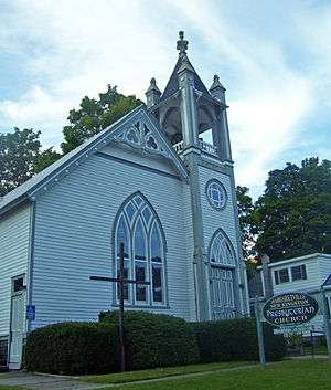 A white church with arched windows and an ornate belfry. In front are a wooden cross and a sign saying "Margaretville New Kingston Presbyterian Church"
