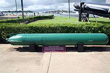 Submarine torperdo on outside display win a naval museum located neat the shore.