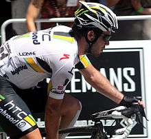A road racing cyclist wearing a black and white jersey with yellow and green trim. His bicycle is only partly visible.