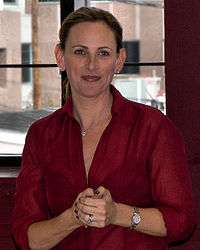 Upper torso of a female with her hands clasped together. She is wearing an unr=buttoned red collared blouse.