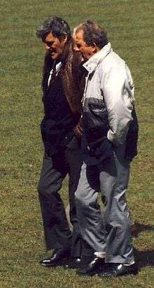 Two middle-aged men, standing on a grass field