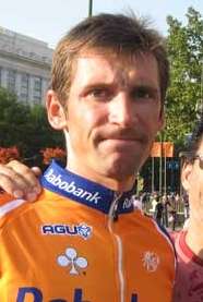 A man in his late twenties, wearing an orange and blue cycling jersey with white trim