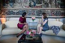 Michelle Obama and Carla Bruni share a laugh while seated on adjacent couches.