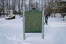 State of Michigan Historical marker with gold text on a green background, standing in a field of snow