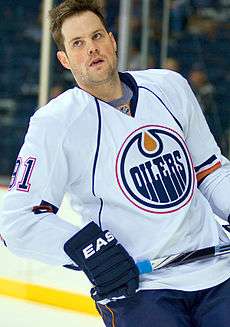 Mike Comrie skating on the ice holding his hockey stick as an Edmonton Oilers team member.