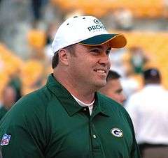 Candid photograph of McCarthy wearing a green Packers polo shirt and white Packers baseball cap.